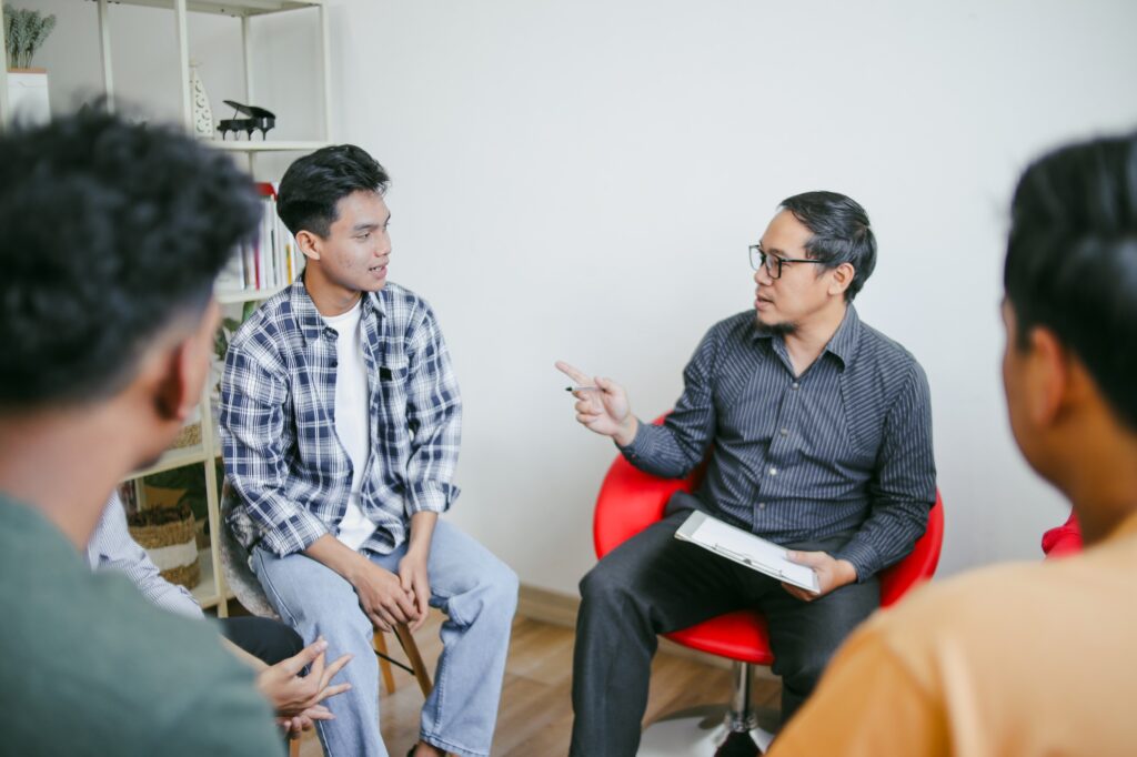 Teenager Students With Young Teacher At Classroom, Talking And Sharing Conversation Together